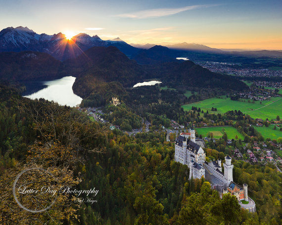 Original fine art photography print of the Neuschwanstein Castle in the foreground and the sun falling behind the Bavarian mountains in the background. 